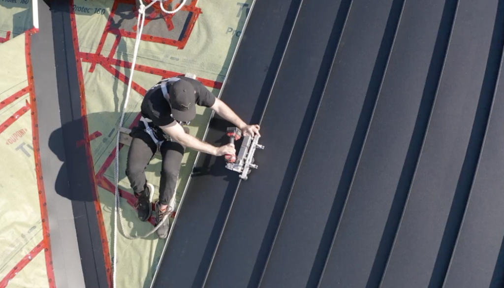 Steel roofing vs metal roofing. Worker fastens steel roof.