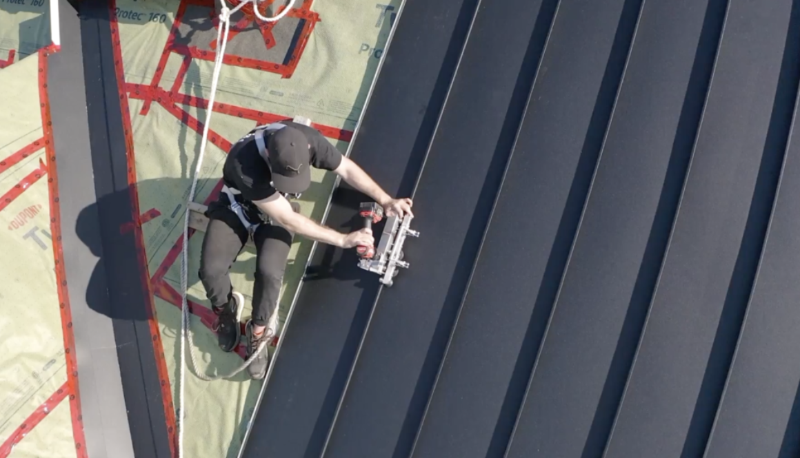 Steel roofing vs metal roofing. Worker fastens steel roof.